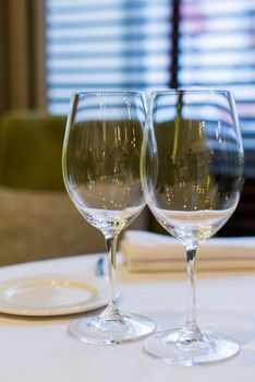 Close-up of two empty wine glasses on a table set for dining indoors, creating an elegant atmosphere.
