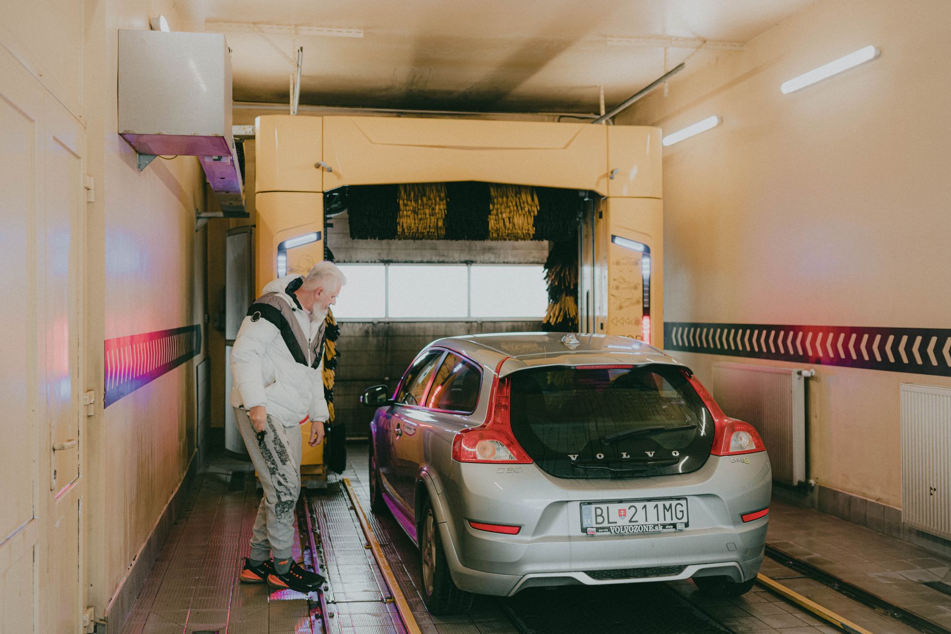 A silver Volvo V40 in an automatic car wash with a man observing nearby.