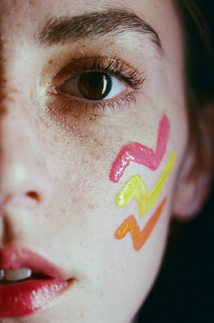 Artistic close-up portrait of a woman with zigzag face paint, focusing on eye and makeup.