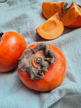 Vibrant ripe persimmons displayed whole and sliced on a textured fabric background.