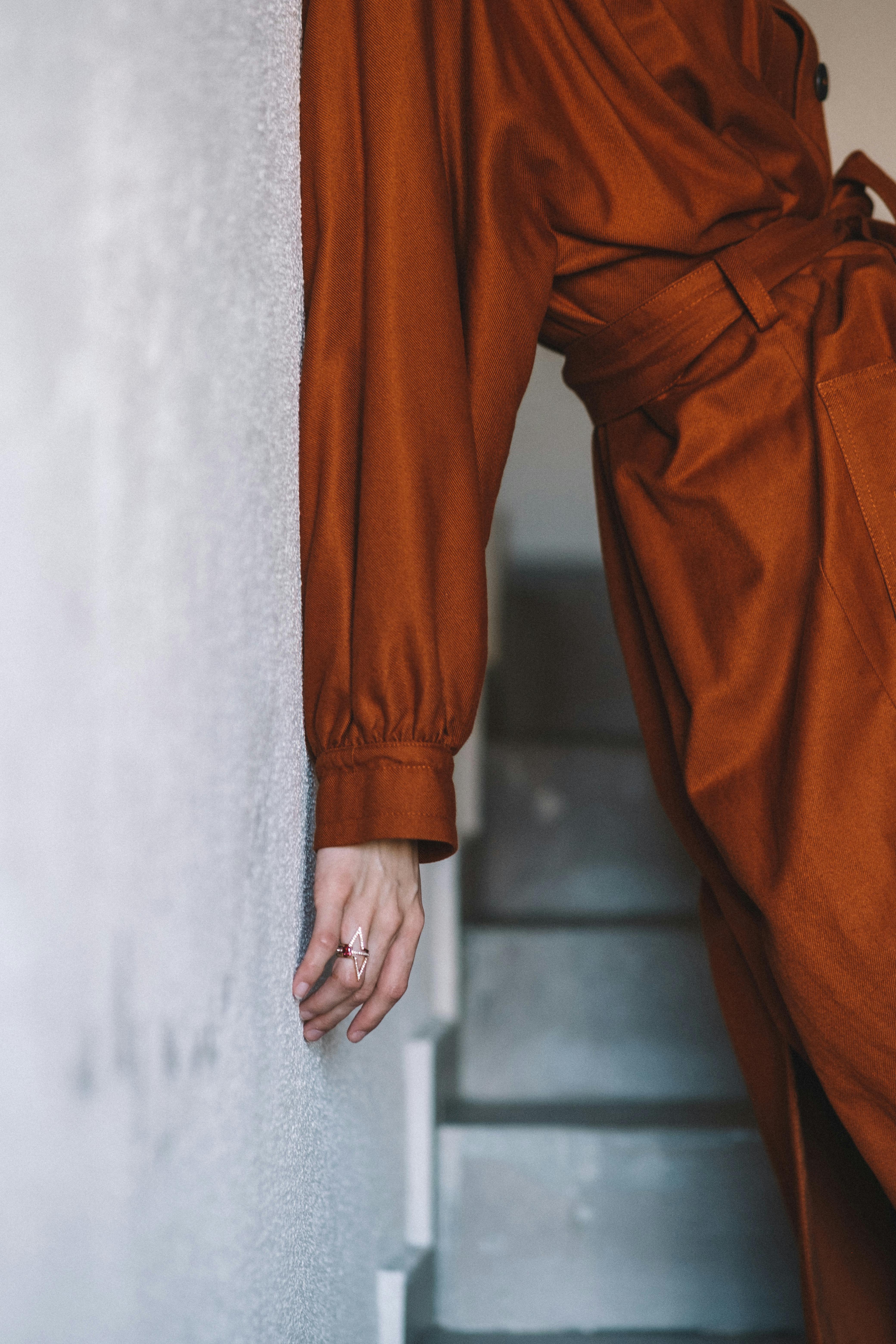 Close-up of a woman leaning on a white wall in an orange dress indoors, capturing modern style.