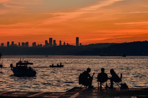 Free A serene sunset view by the water with silhouetted people and Istanbul skyline in the background. Stock Photo