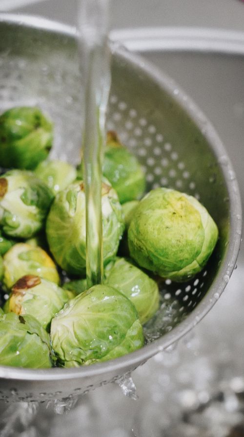 Free Close-up of fresh Brussels sprouts being washed in a strainer, emphasizing healthy food preparation. Stock Photo