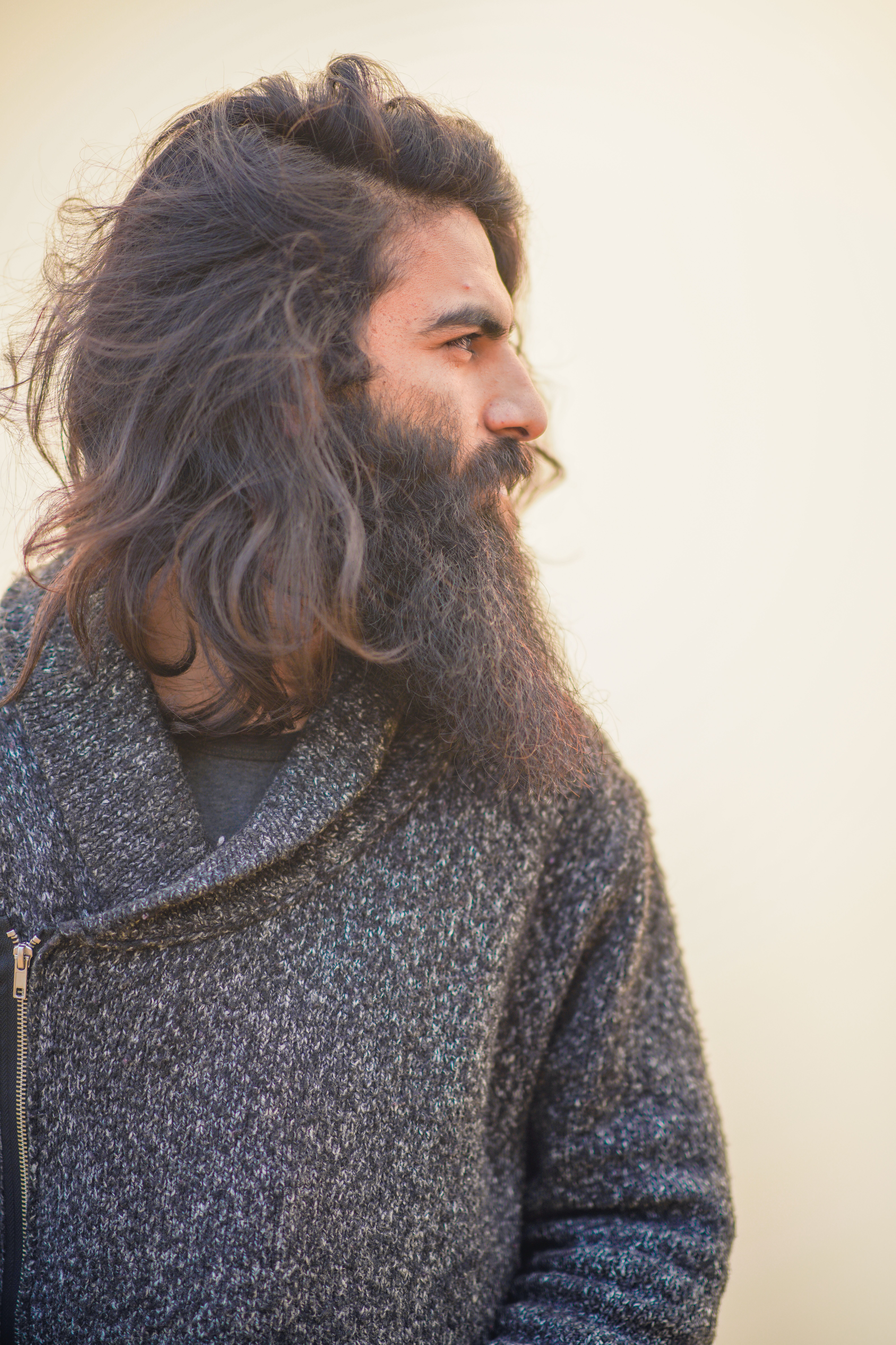 Portrait of a bearded man with long hair in a textured sweater looking sideways.