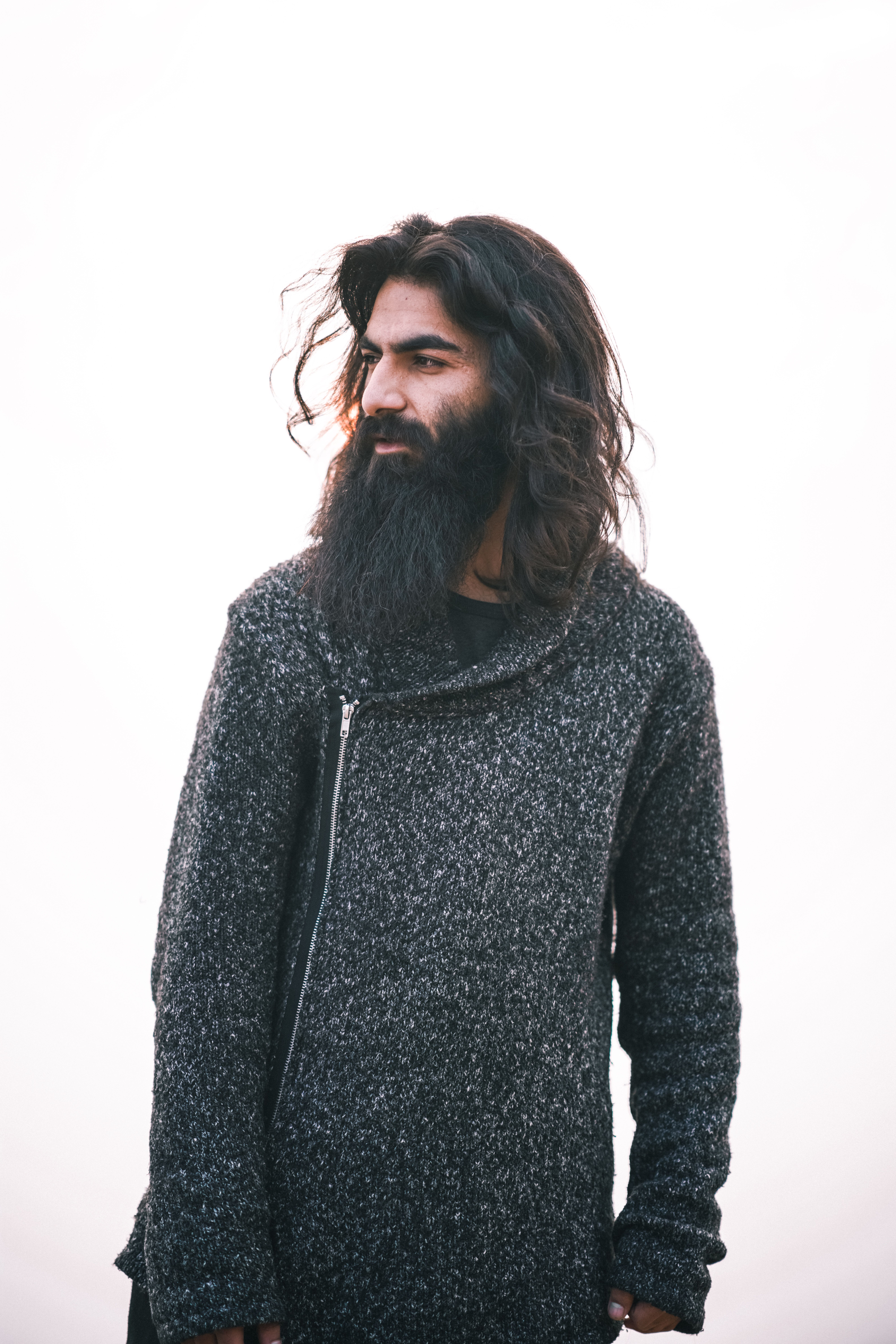 Stylish portrait of a bearded man with long hair, wearing a warm sweater against a bright backdrop.