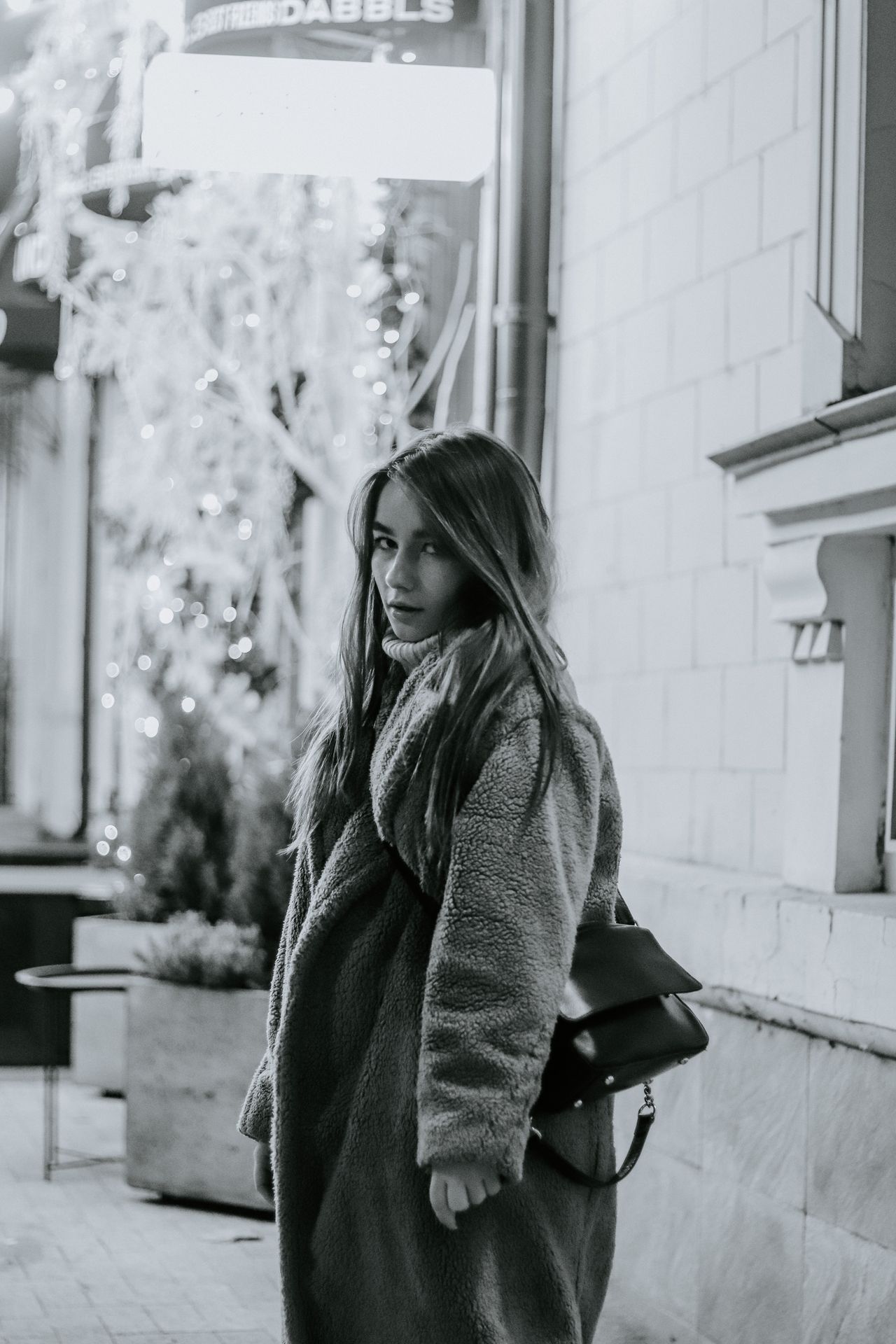 Woman in a fuzzy teddy coat on a city street at night