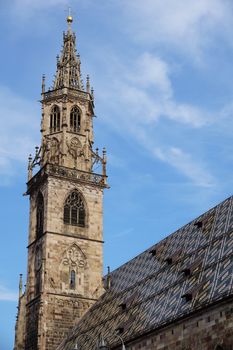 Stunning view of the Gothic-style Bolzano Cathedral tower against a blue sky in Italy.