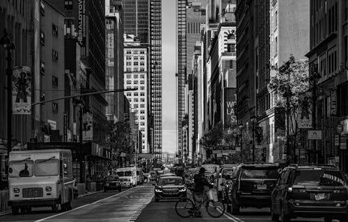 Grayscale Photo of a Person Crossing the Street with a Bicycle