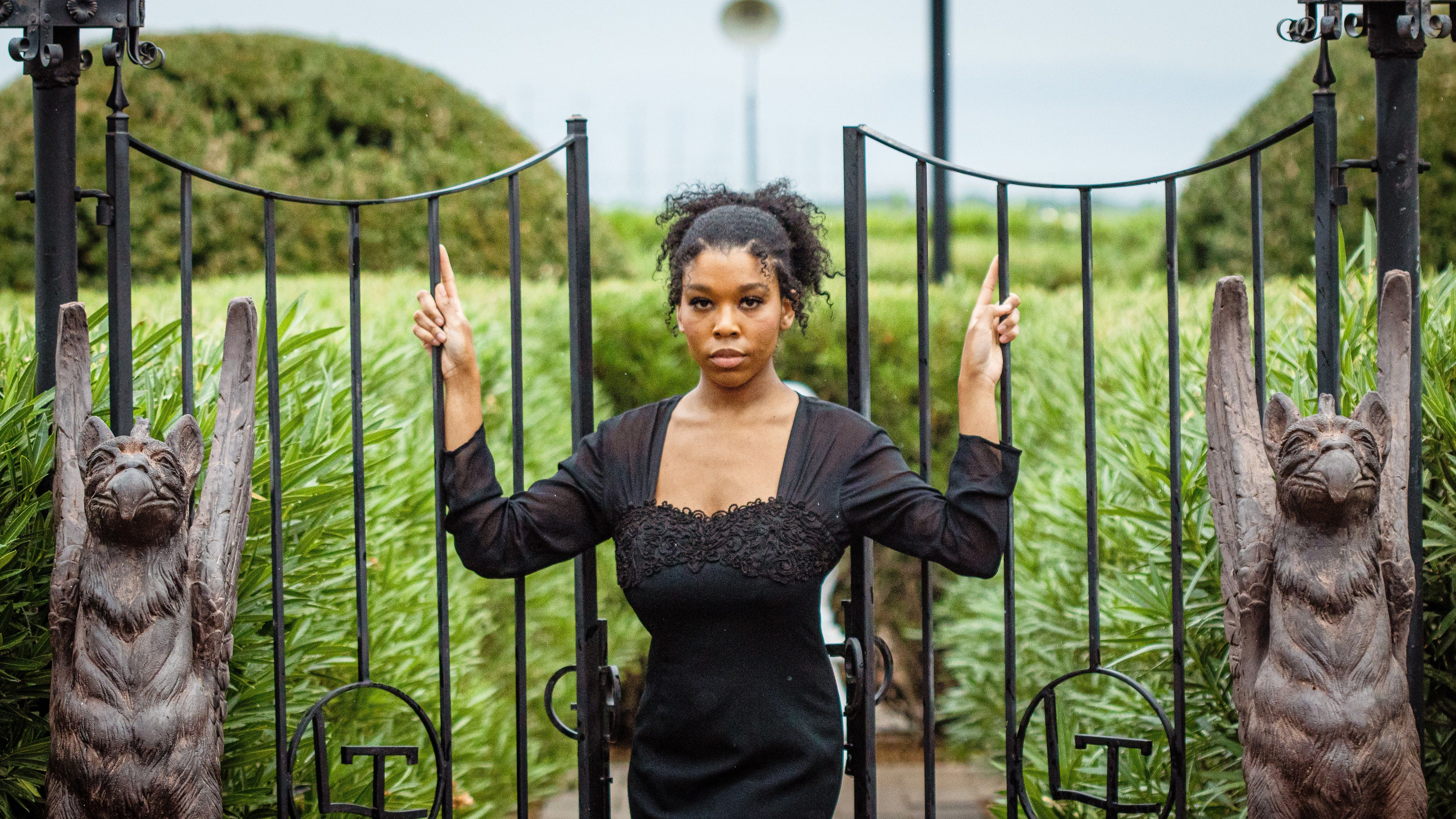 Portrait of a stylish woman in a black dress posing by sculpted gates outdoors in Buckeye, AZ.