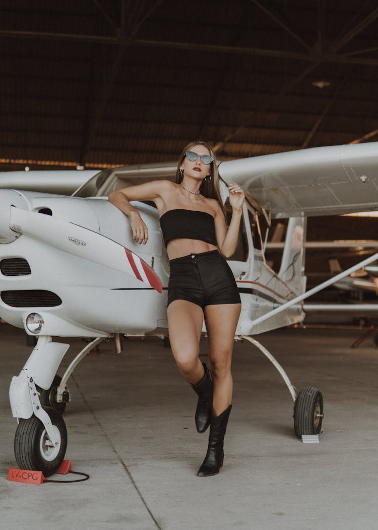 A Woman In A Stylish Outfit Leaning On An Airplane