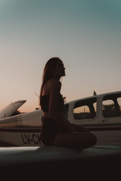 Free A woman in silhouette sits on an airplane wing during a scenic sunset. Perfect for travel and adventure themes. Stock Photo