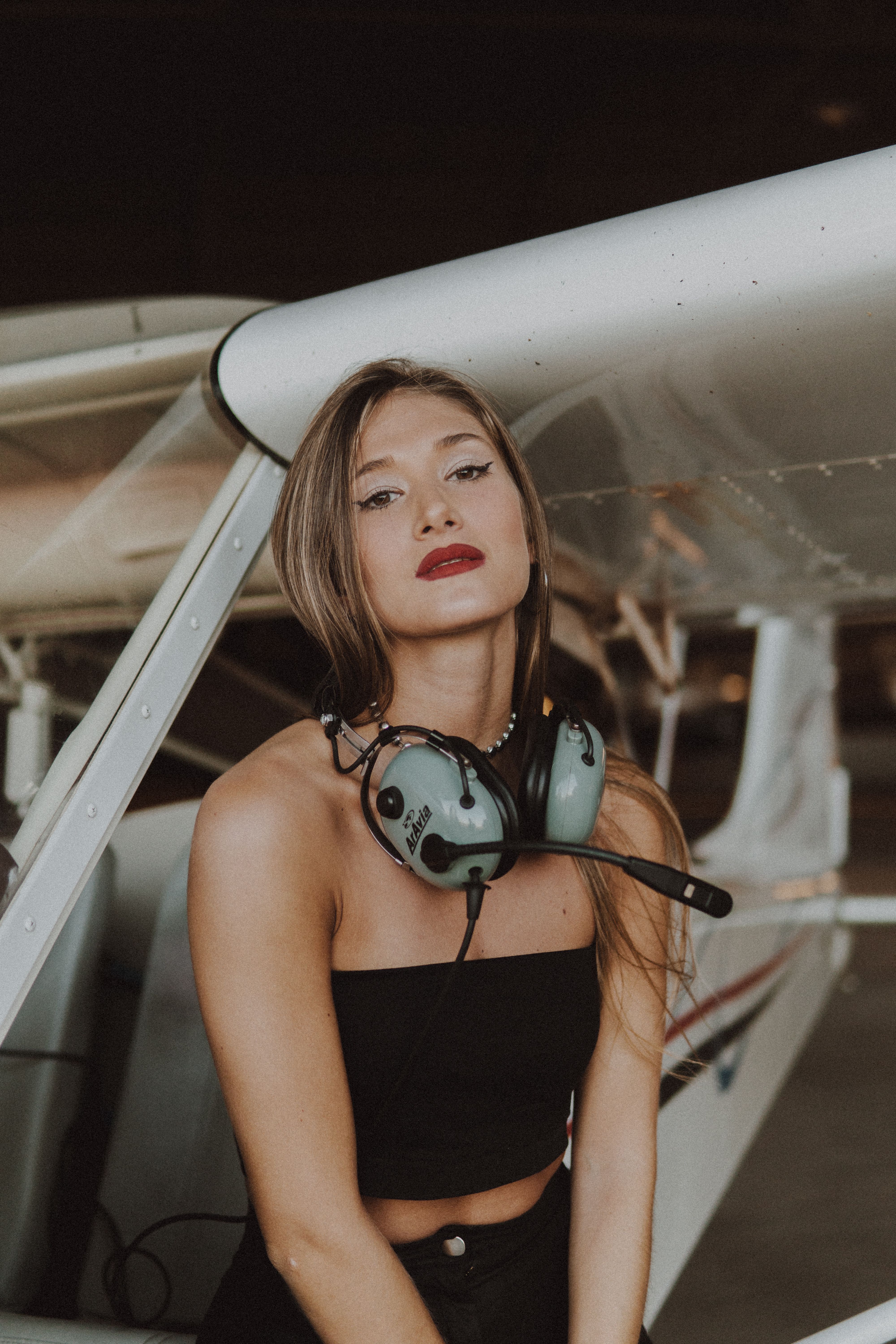 Caucasian woman in stylish attire with headset near a small airplane.