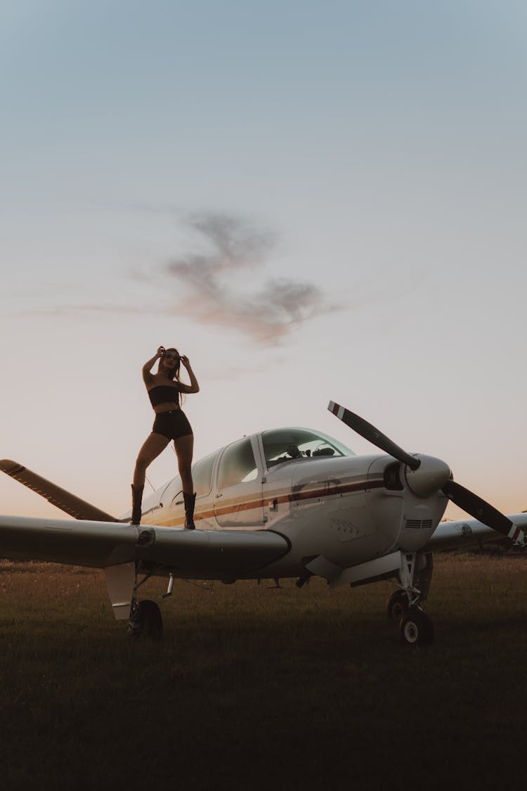 A Woman In A Stylish Outfit Standing On An Airplane Wing