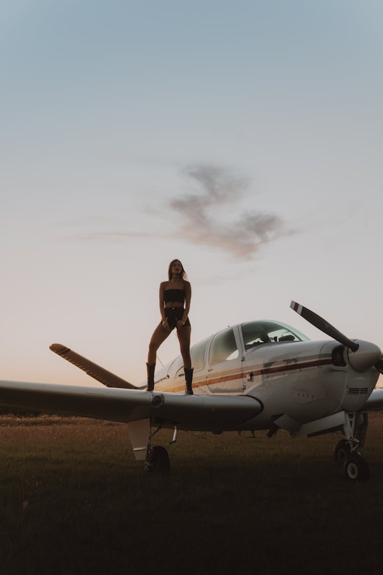 A Woman In A Stylish Outfit Standing On An Airplane Wing