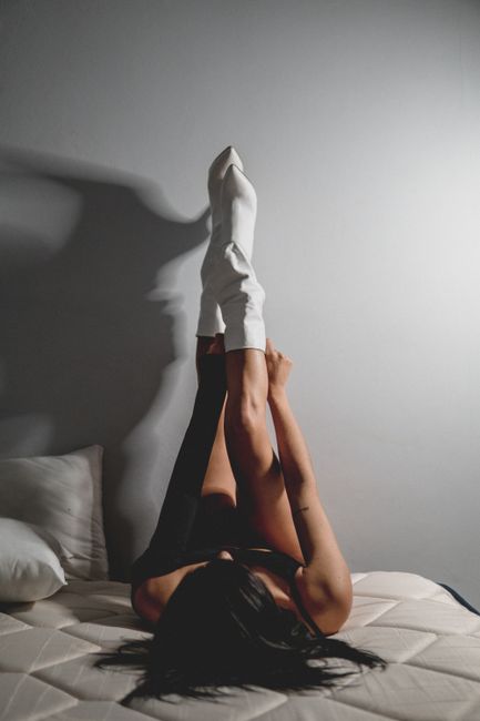 Artistic photo of woman's legs in white boots raised on a bed.