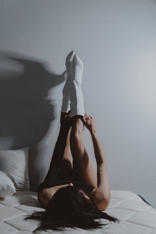 Free A Woman Lying in Bed Putting on Her White Boots Stock Photo