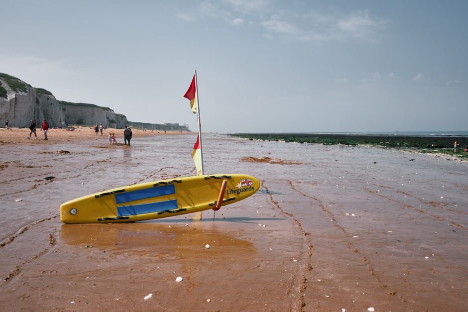 A lifeguard board on a sandy beach in England with people enjoying the coast.