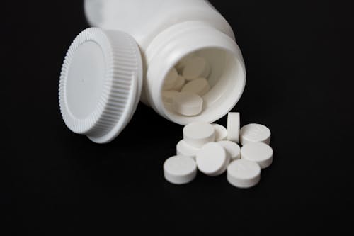 White Container and Pills on Black Surface