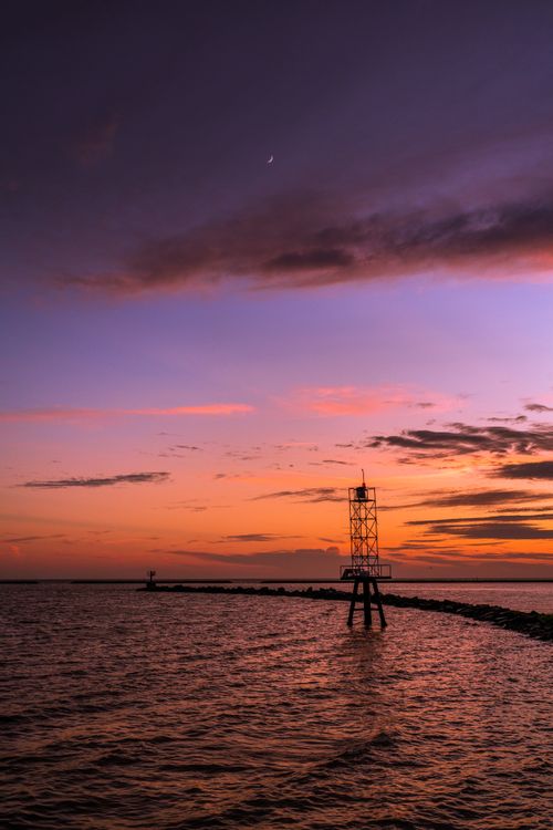 Free Tranquil ocean sunset with beacon and twilight sky, perfect for scenic backgrounds. Stock Photo