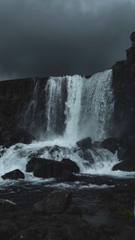 A powerful waterfall in Iceland under a dramatic stormy sky, showcasing nature's raw beauty.