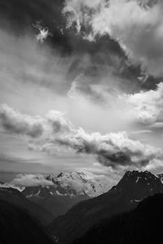 Monochrome view of rugged mountains under a dynamic cloudy sky.