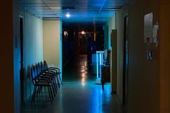Atmospheric view of a quiet, dimly lit hospital hallway with chairs and signs.