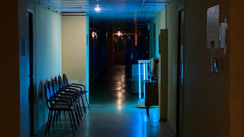 Atmospheric view of a quiet, dimly lit hospital hallway with chairs and signs.