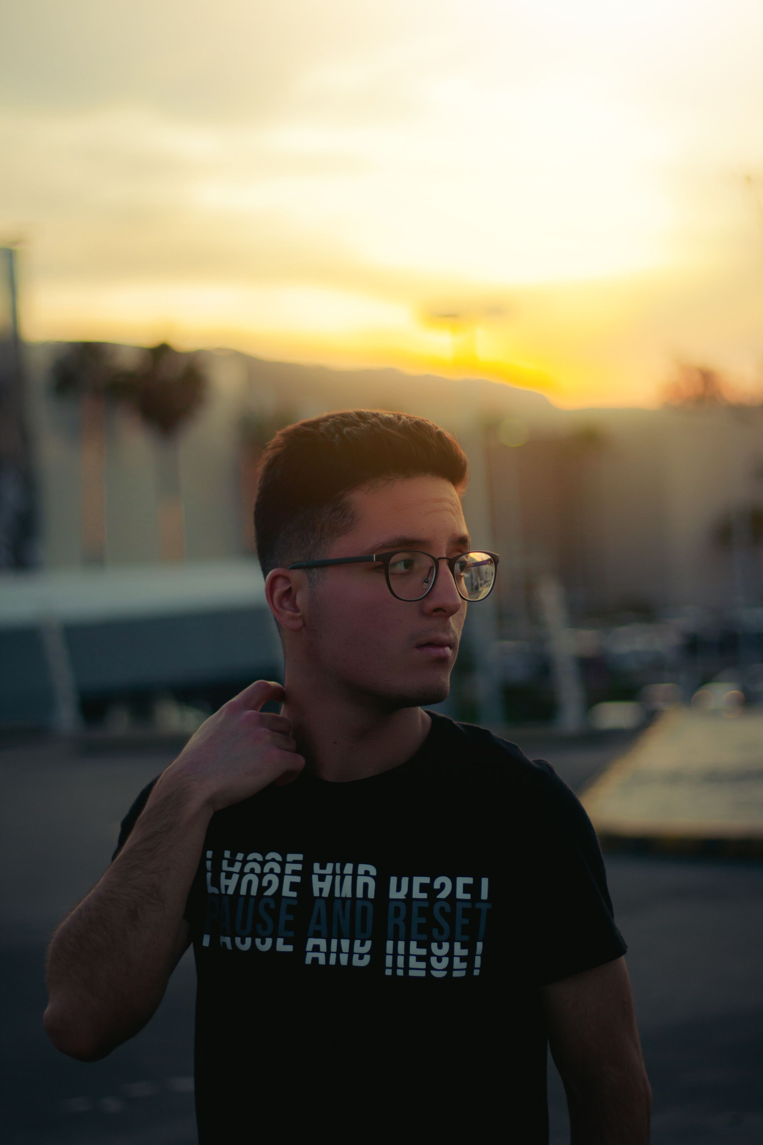 Young man wearing glasses looking thoughtful during sunset outdoors.