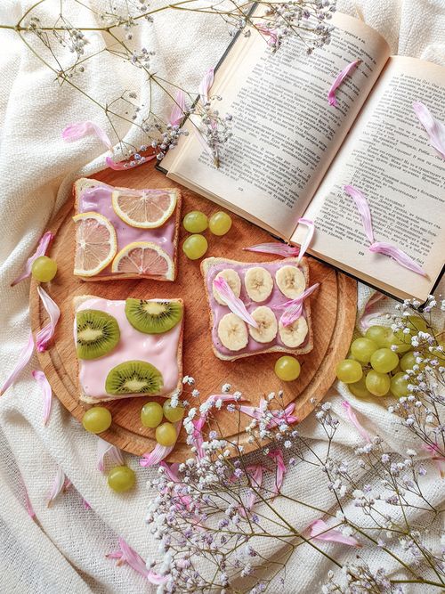 Free Artistic flat lay featuring fruity toast, open book, and flowers for an inspiring breakfast scene. Stock Photo