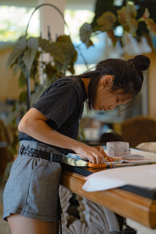 Woman in Black Shirt Cutting Fabric on a Wooden Table