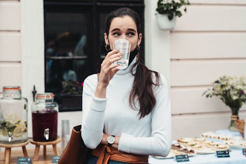 Woman in White Long Sleeve Shirt Drinking from Clear Drinking Glass