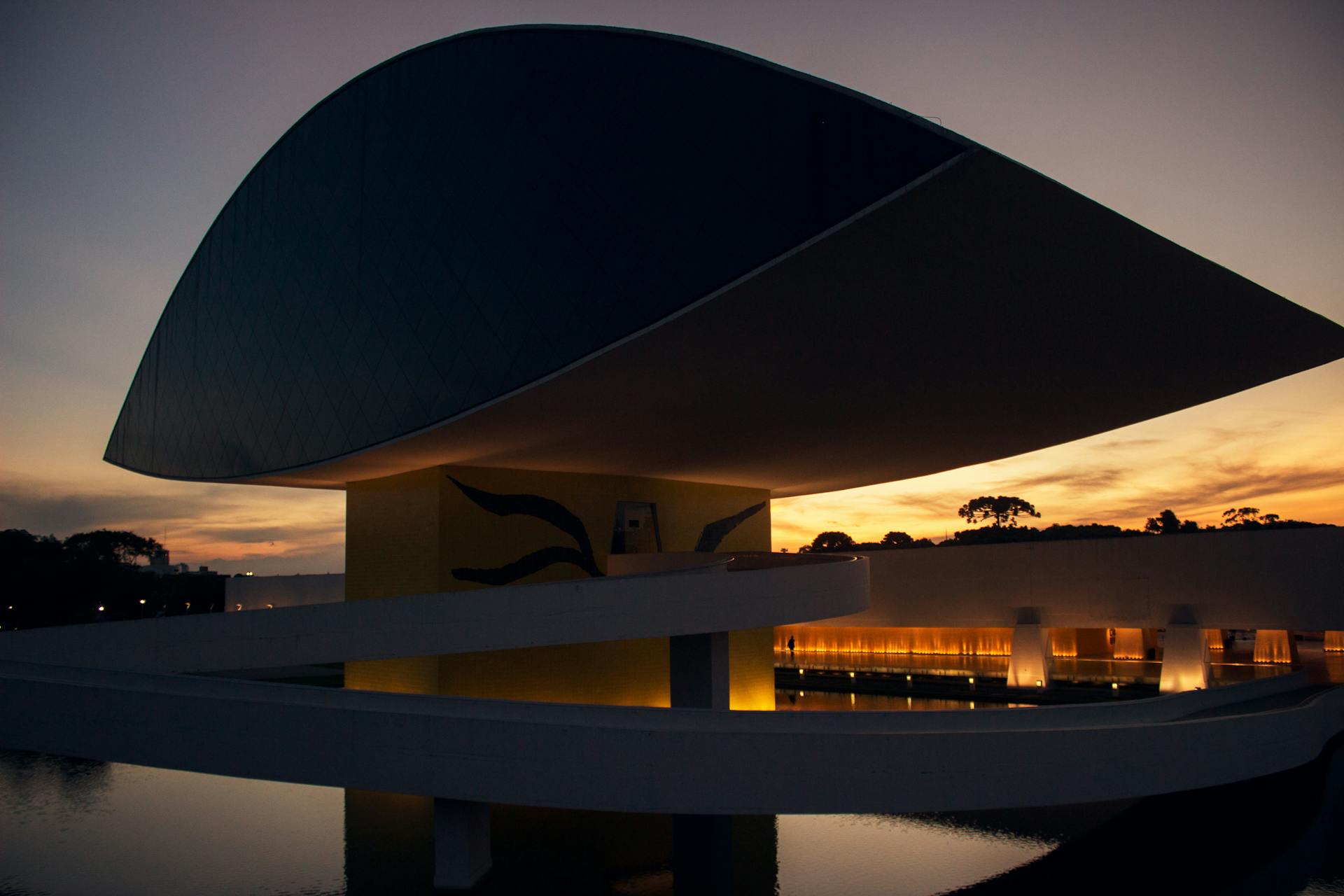 Stunning sunset view of a modern architectural landmark in Brazil, reflecting in water.