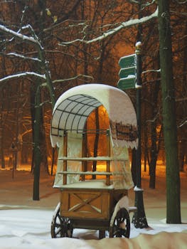 A rustic wooden cart covered in snow stands in a tranquil, snowy forest at night.