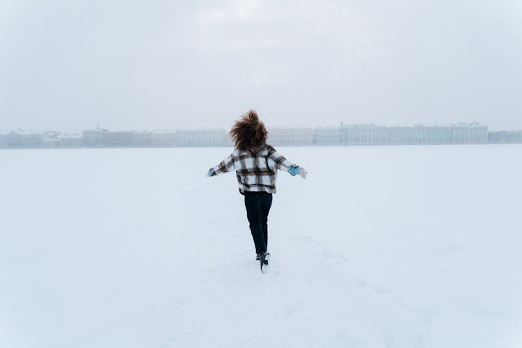 Woman Running Through Snow Field With Arms Stretched Out