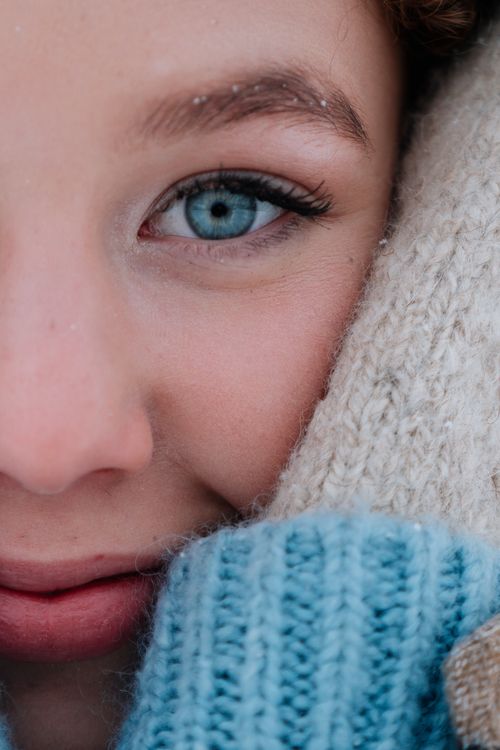 Free Half-face portrait of a woman smiling in winter clothing, showcasing bright blue eyes. Stock Photo