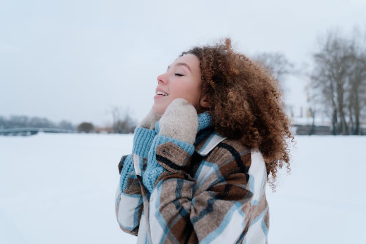 Woman Wearing Winter Clothes Standing In Snow Field Touching Face