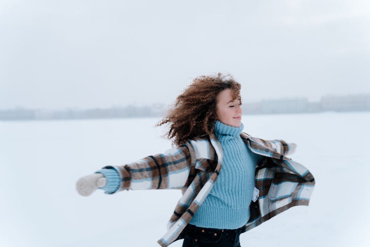 Woman Running Through Snow Field With Arms Stretched Out