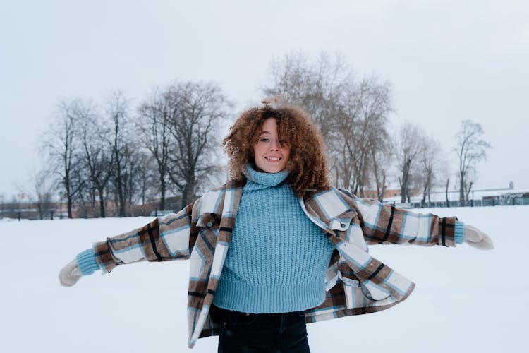 Woman With Curly Hair Wearing Winter Clothes Playing In Snow Field