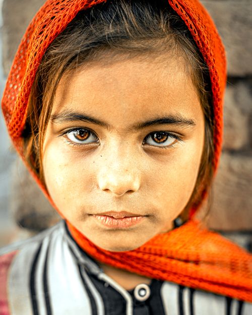Free Close-up of a young girl in a vibrant orange headscarf outdoors in Pakistan. Stock Photo