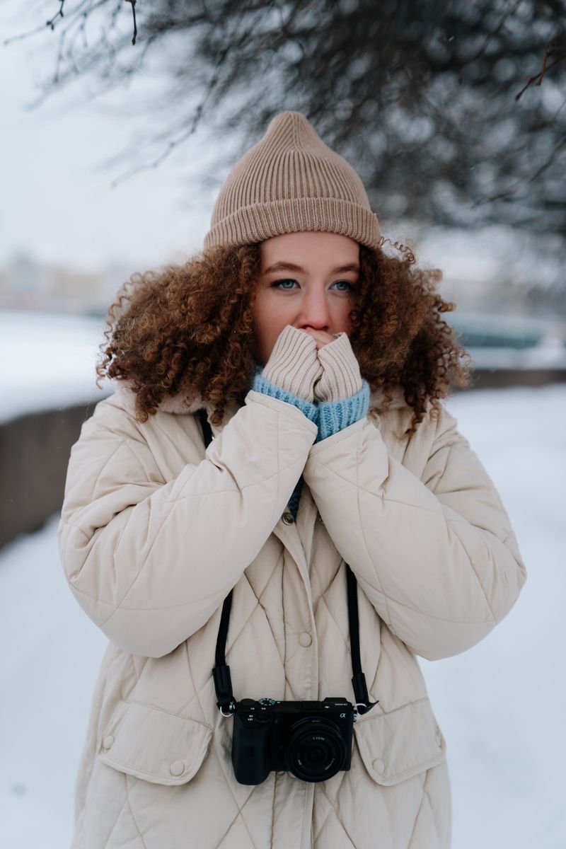 Woman in winter jacket and beanie with camera in snow