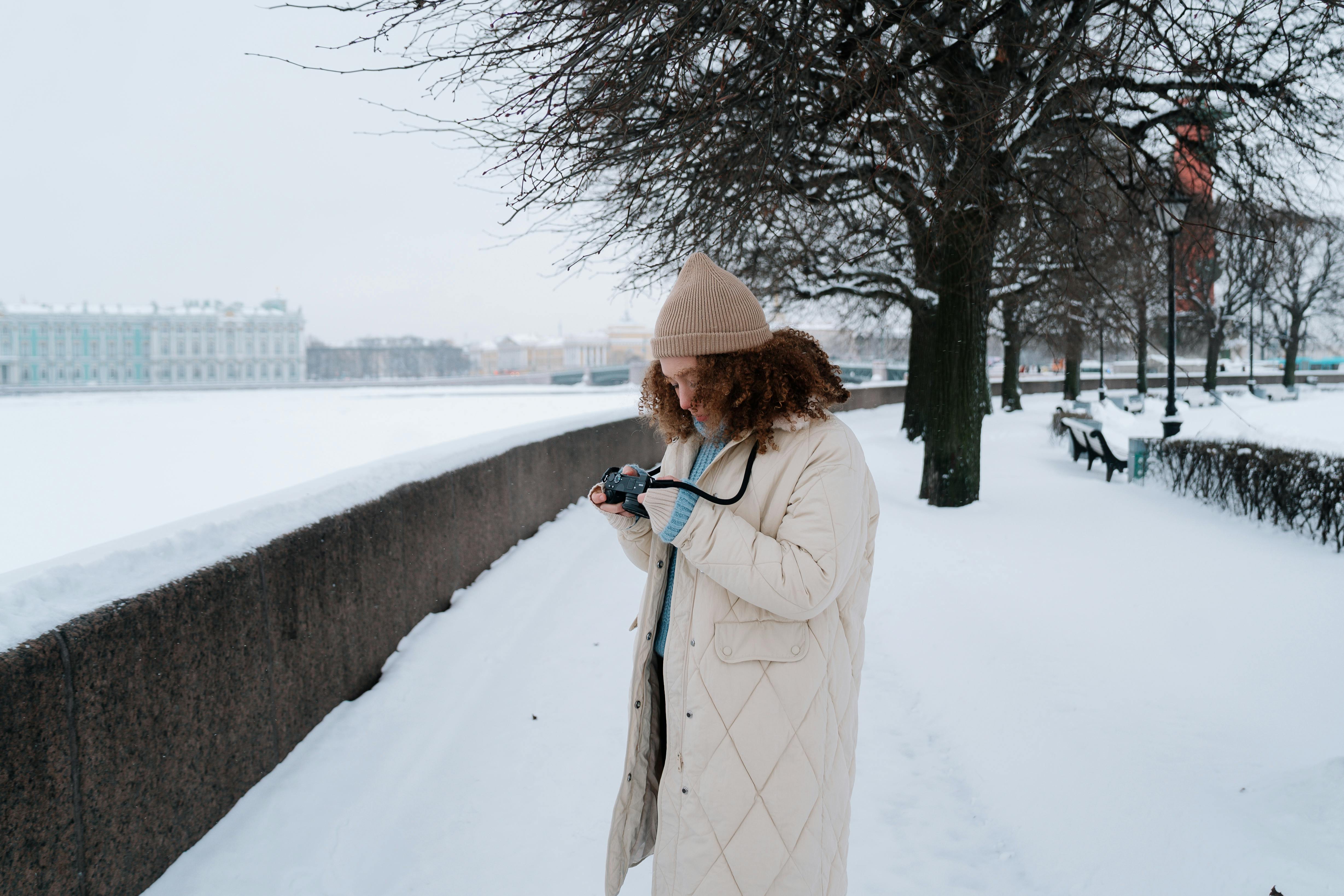 Curly Haired Woman in Jacket Looking at Analog Camera