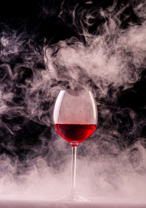 Free Elegant red wine glass enveloped in swirling smoke creating a dramatic effect. Stock Photo