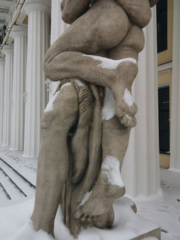 Close-up of a snow-covered sculpture outside a classical building in winter.