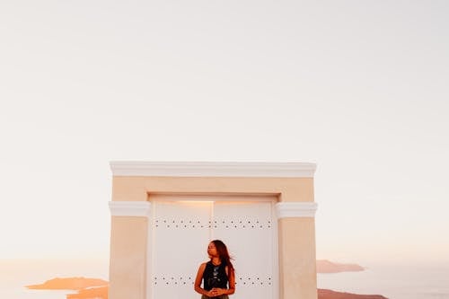 Woman Wearing Black Sleeveless Top Posing in Front of White Wooden Door