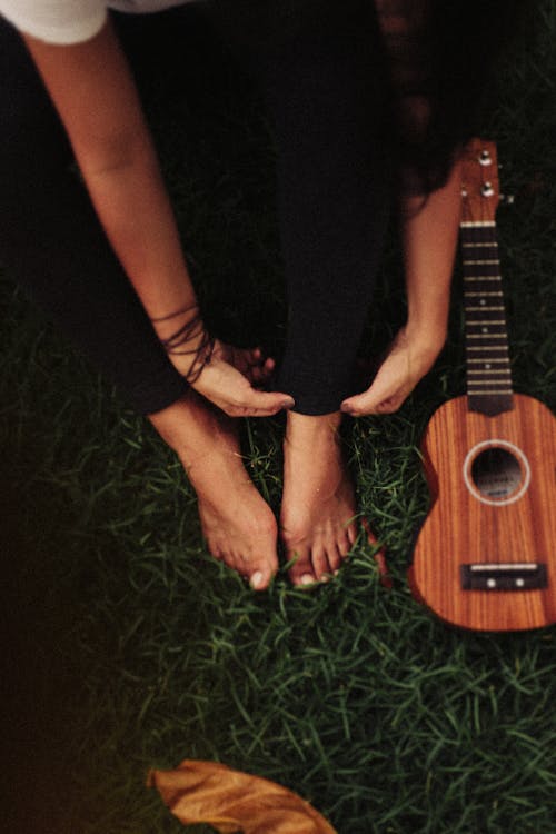 Person Sitting on Green Grass Field Beside Ukulele