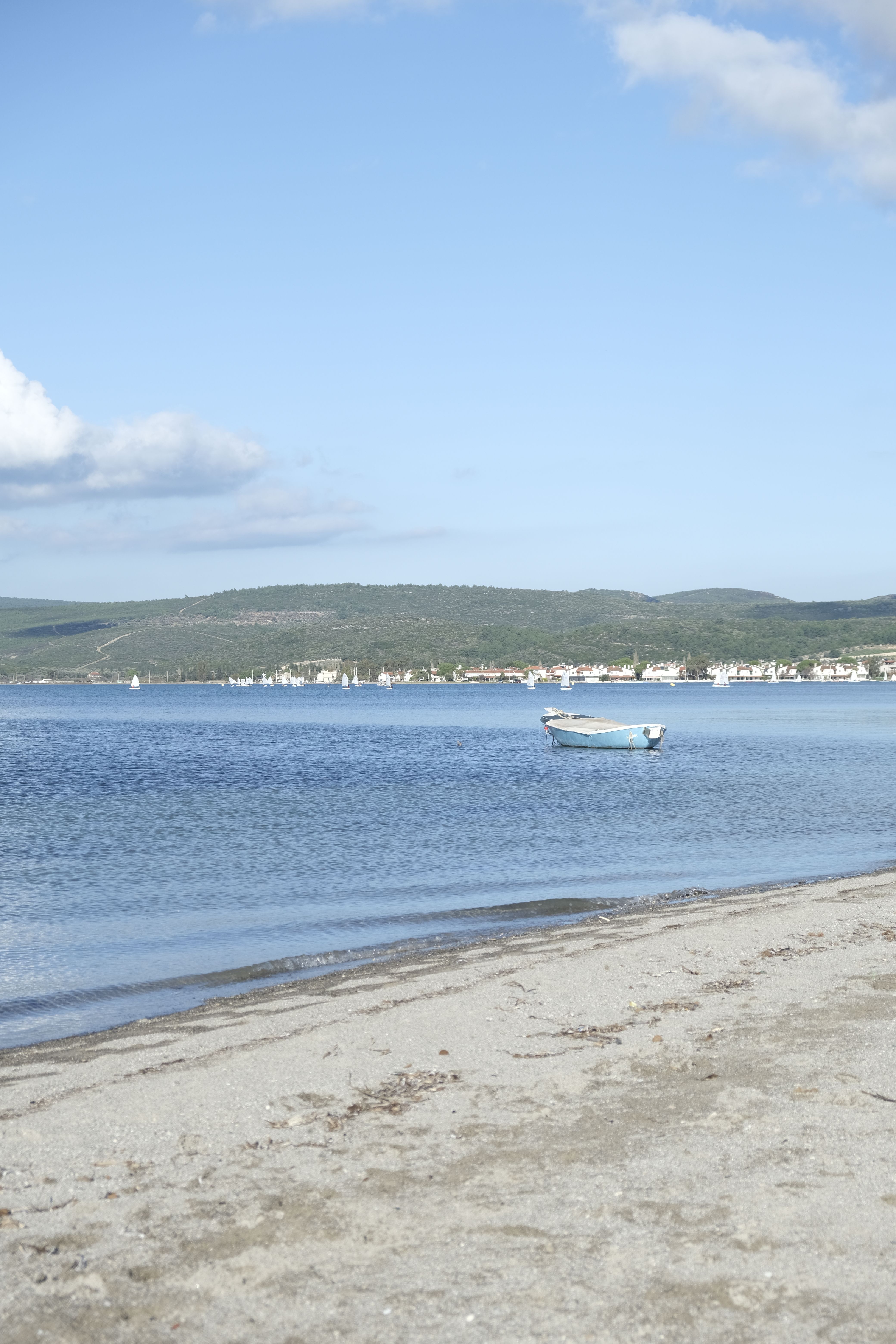 Serene coastal landscape of Urla beach with a boat on clear blue waters under a bright sky in İzmir, Turkey.