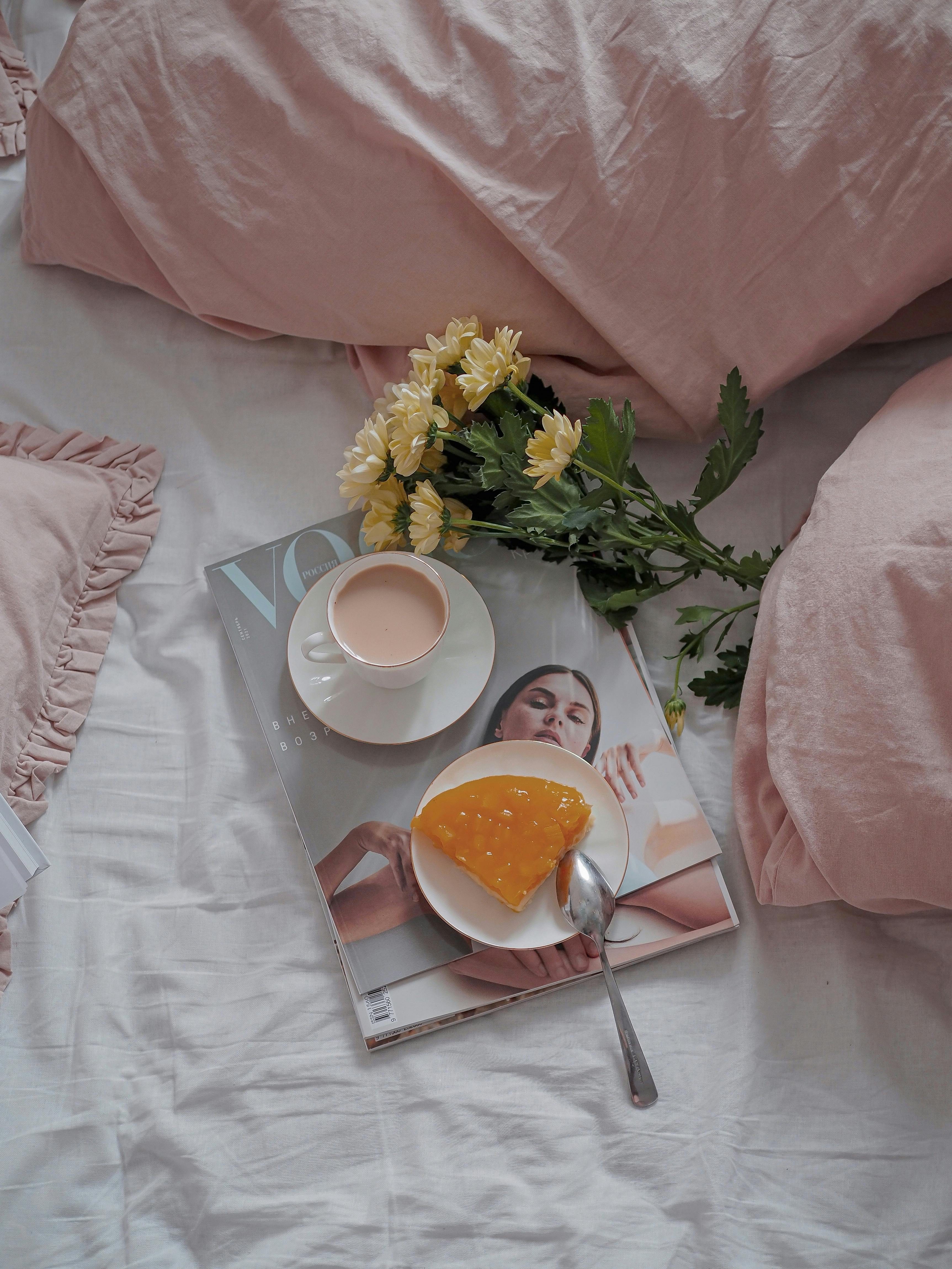 A stylish breakfast setup featuring cake, coffee, and flowers on a bed.