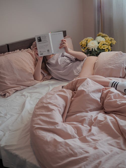 Free Woman Lying on Bed Reading Book Stock Photo