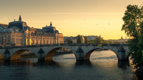 Free Scenic view of a historic arch bridge in Paris at sunset, showcasing the Seine River with the Musée d'Orsay in the background. Stock Photo
