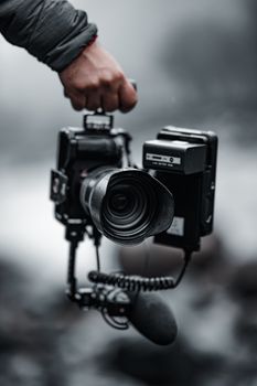 Close-up of a photographer's hand holding a professional DSLR camera with a lens, outdoors.